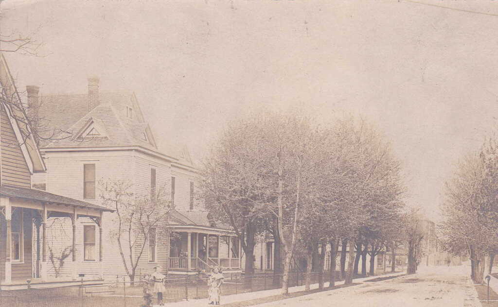 Street lined with houses and rows of trees, with children on the sidewalk