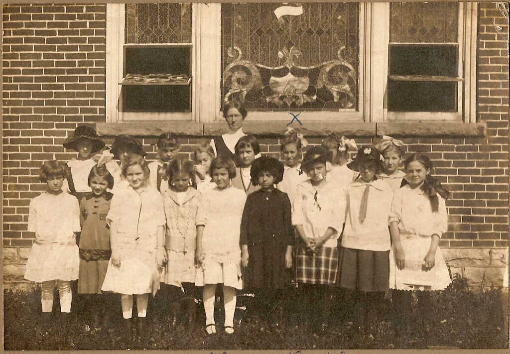 Class photo with elementary school girls and their Teacher in front of stained glass window